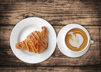Top view of coffee and croissant breakfast on a wood table top. French pastry and cappuccino in a coffee shop.
