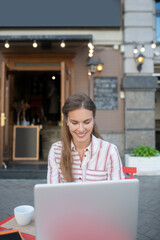 Brown-haired female working on her laptop in open air cafe