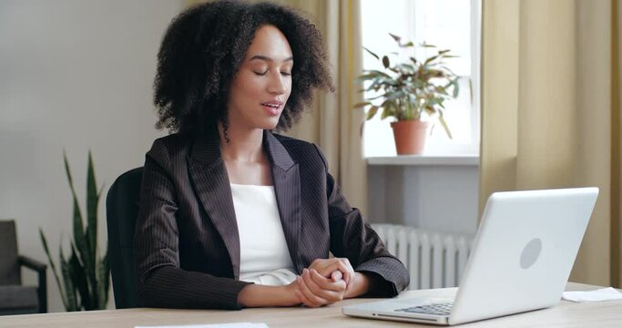 Joyful young mixed race businesswoman freelancer in black jacket holding online video call with friends or clients using laptop application, working interpreter remotely from home, teaching languages