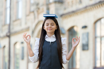 Calm the mind. Little child do meditation outdoors. Small girl do mudra hands holding book on head....