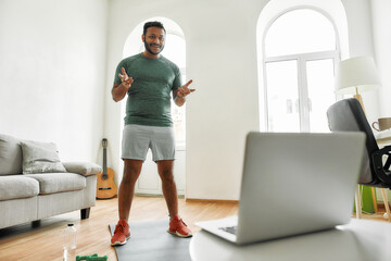 Stay in touch. Full length shot of male fitness instructor greeting viewers while streaming, broadcasting video lesson on training at home using laptop. Sport, online gym concept