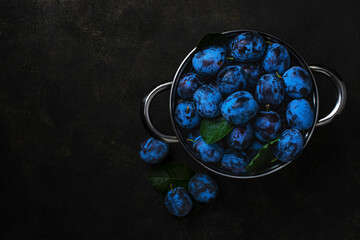 Pan with fresh plums on a dark table. View from above.