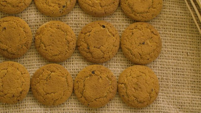 Close up oatmeal cookies and ears of ripe rye. Raw cereals and oatmeal cookies macro on burlap background. Camera slowly moving on slider, dolly shot, top view