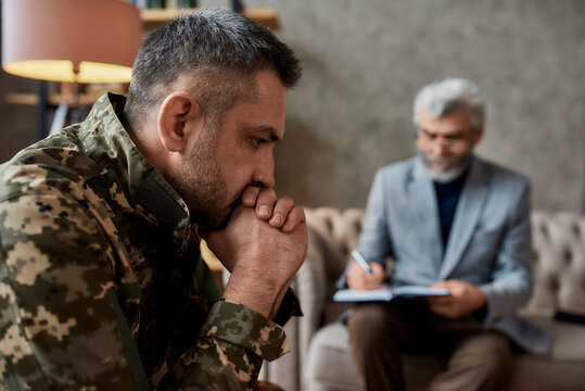 Need help. Middle aged military man looking thoughtful during therapy session with psychologist. Soldier suffering from depression, psychological trauma. PTSD concept