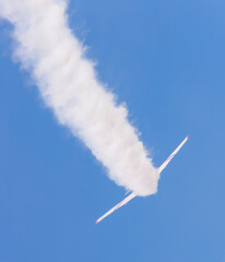 Airplane banking and leaving a smoke trail on blue sky