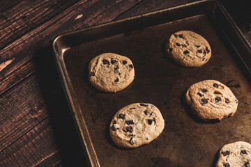 Fresh baked chocolate chip cookies still in the baking pan on a wooden table top.