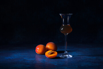 Apricot brandy in shot glass with fresh ripe apricots on blue table with dark background.
