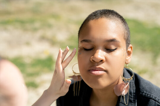 Close-up Of Unrecognizable Woman Putting On Glitter Makeup To Black Girl Outdoors