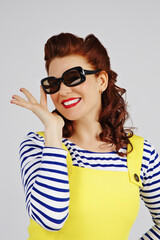 Naklejka premium jeune et jolie femme brune pin up souriante avec une mini robe jaune d'été et un tee-shirt marin ligné avec des lunettes solaires sur fond isolé de studio 