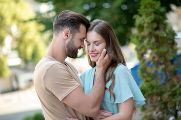 Bearded male hugging female in blue dress, holding her chin