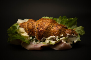 Salty tasty breakfast with a croissant with ham, cheese and salad on a black background. Italian snack.