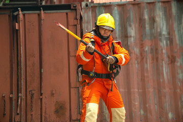 A portrait of Asian male fireman in orange protective clothing, mask and helmet with an ax standing front of building.