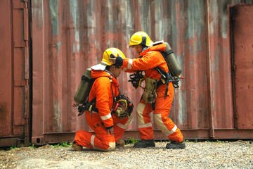 The portrait of Asian firefighters are wearing orange fire protection uniform mask and helmet front of building.