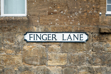 A street sign in the centre of the frame set against a brick stone wall.  The road sign says Finger Lane in traditional black on white UK town sign style