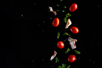 Falling bacon, cherry tomatoes, parsley on a black background with water drops, freeze in motion, cooking and recipe books, banner