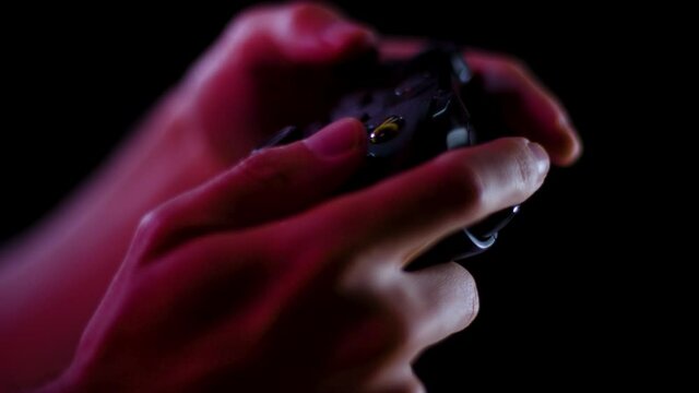 Playing video games in a darkened room with a black background close up on a controller buttons playing slowly