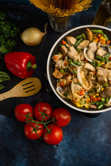 Meat is fried in a pan with vegetables on a background of fresh vegetables on a blue background, top view