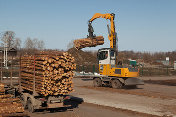 An industrial loader loads logs into a conveyor at a sawmill
