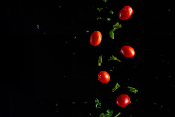 Falling cherry tomatoes with parsley and onions, herbs, and drops of water, freeze in motion on a black background