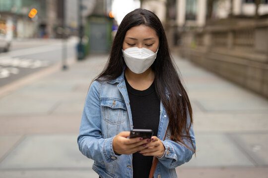 Young Asian woman walking street wearing a mask texting on cellphone