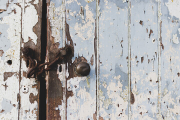 Old wooden door with peeling white paint closed with a rusty chain.