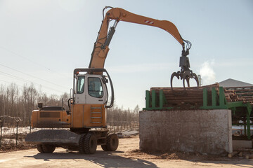 An industrial loader loads logs into a conveyor at a sawmill