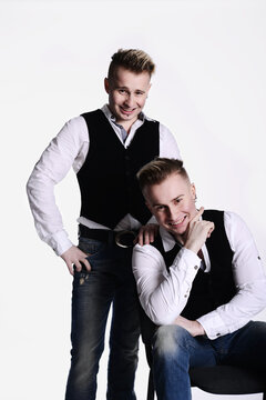 two twin brothers in gangster style posing. hats, vests, white shirts. white background.
