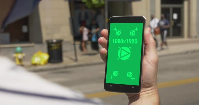 An over-the-shoulder shot of a man in a face mask using or talking on a green screen smartphone. Optional tracking points for screen replacement.  	