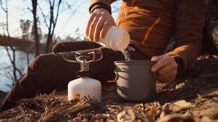 Hands man Close-up pours water from flasks into a pot for boiling water on a gas tourist burner camping forest