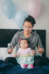 Madre y su bebé felices celebrando cumpleaños en la casa durante la cuarentena. Madre e hija celebran con globos y pompas de jabón.