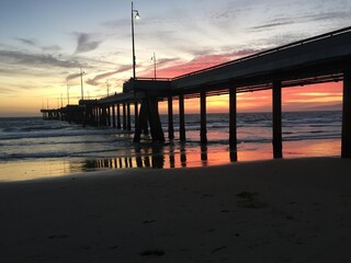 Fototapeta premium Landscape view of pier over sandy beach shore at sunset