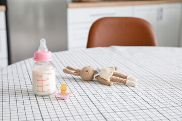 Bottle of milk for baby, toy and pacifier on table