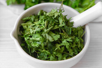 Mortar with dry parsley on table