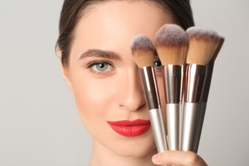 Young woman with makeup brushes on light background