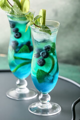 Glasses of tasty blue mojito cocktail on color background