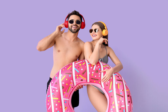 Young couple with headphones and inflatable ring on color background