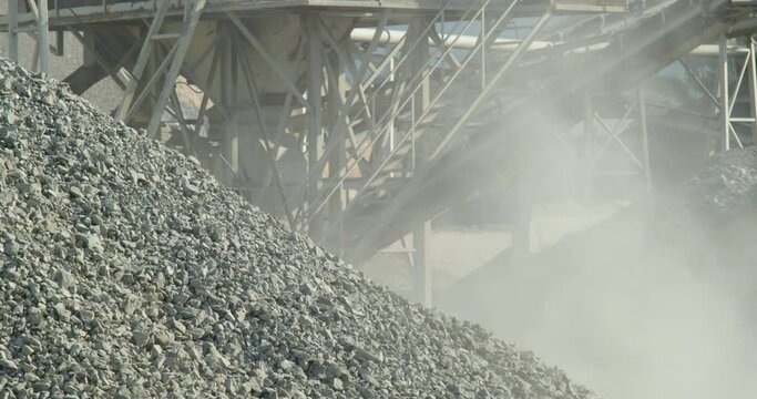 Bulldozer operator loading and transporting stones in scoop during the separation of building materials in stone crusher plant. Excavator at work in the quarry. Dust and smoke rising