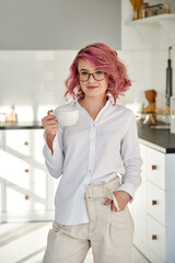 Smiling young stylish fashion hipster teen girl pink hair wears white shirt glasses holding cup...