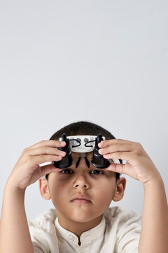 Vertical shot of a boy in headband magnifying glass looking at camera