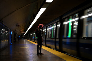 Redhead girl waiting for the train standing alone in a subway station wearing a red hat and a travel backpack