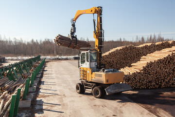 An industrial loader loads logs into a conveyor at a sawmill