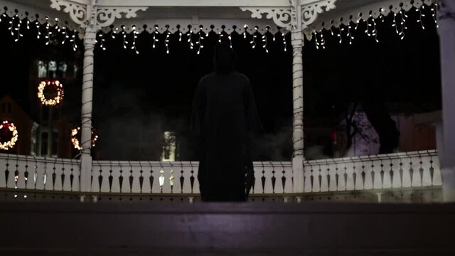 Tilt up WIDE-SHOT of someone in a Grim Reaper costume in front of Christmas lights