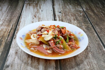 Traditional spicy mixed salad with chopped squid, pork sausage, minced pork, chilly, and tomato seasoning with lime juice and fish sauce on the plate. Famous spices street food menu in Asia.