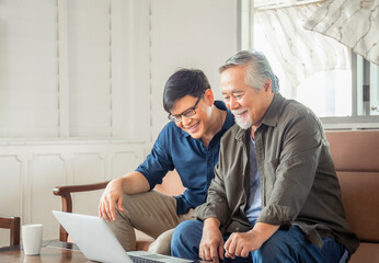 Happy senior asian father and adult son using laptop talking on video call in living room