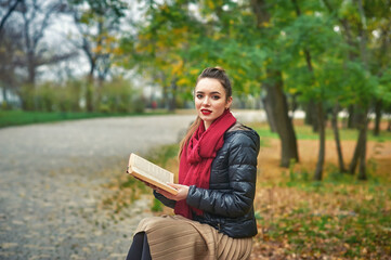 Portrait of a young woman with a book in an autumn Park . Reading fiction in the open air