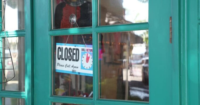 Female small business owner turning an open sign over to closed while wearing a face mask; COVID-19 pandemic theme