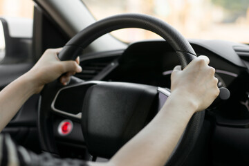 Female hands on the steering wheel of a car while driving. Against the background, the windshield and road,Close-up of a woman's hand driving a car