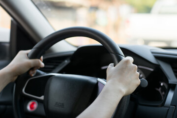 Female hands on the steering wheel of a car while driving. Against the background, the windshield and road,Close-up of a woman's hand driving a car