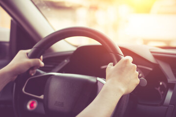Female hands on the steering wheel of a car while driving. Against the background, the windshield...