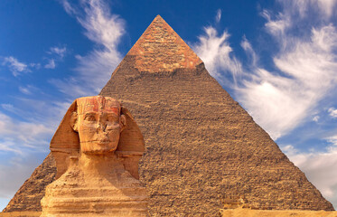 Giant statue of Great Sphinx on the background of the oldest and largest Pyramid of Giza (Pyramid of Cheops), west bank of Nile river, Cairo, Egypt; majestic atmosphere and expressive cirrus clouds